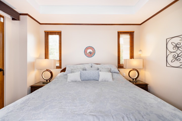 A neatly made bed with gray bedding, two lamps, and two windows in a cozy bedroom.