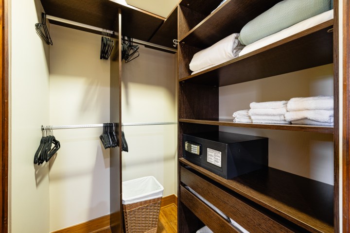 Hotel closet with hangers, shelves, towels, a safe, and a laundry basket.
