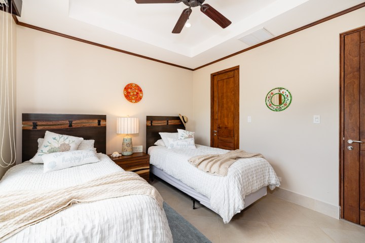 Two twin beds with white bedding, wooden headboards, and a nightstand in a room with a ceiling fan.
