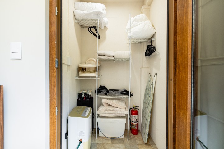 Small utility closet with shelves, fire extinguisher, humidifier, ironing board, and towels.