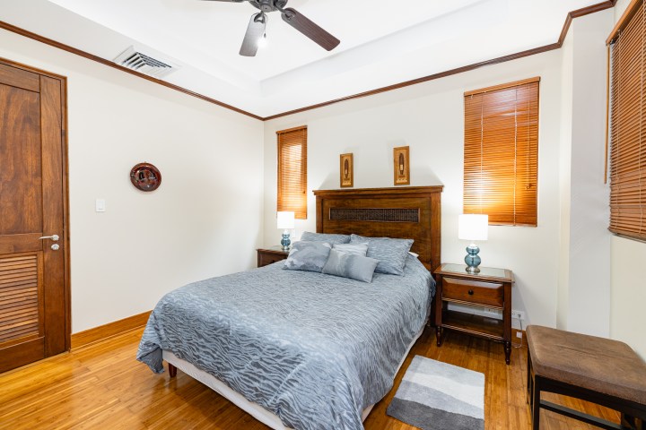 Cozy bedroom with wooden bed, blue bedding, two lamps, and wooden blinds.