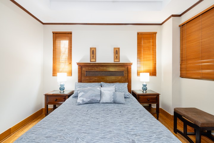 Cozy bedroom with a wooden bed, side tables, lamps, and window blinds.