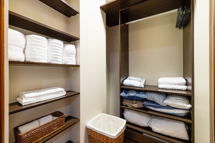 Linen closet with folded towels on shelves and a laundry basket.