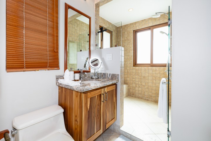 Bathroom with wooden vanity, marble countertop, mirror, shower, and window.