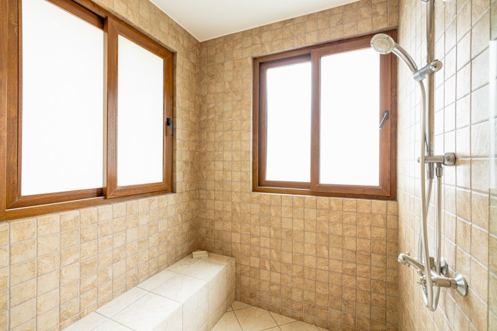 Tiled shower area with two windows, wall-mounted showerhead, and a bench.
