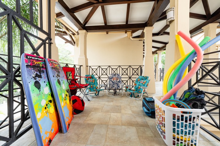 Covered patio with beach chairs, boogie boards, pool noodles, and a basket of beach gear.