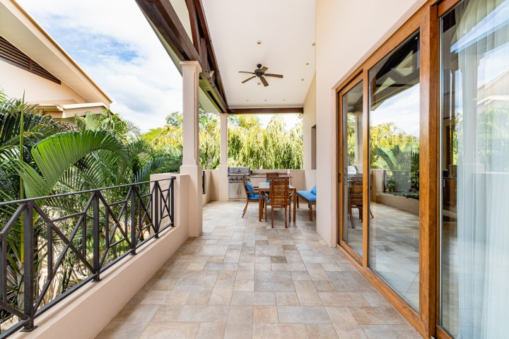 Outdoor patio with wooden furniture, ceiling fan, and lush greenery surrounding.