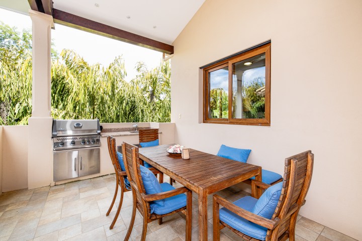 Outdoor patio with wooden table, blue cushioned chairs, and a stainless steel grill.