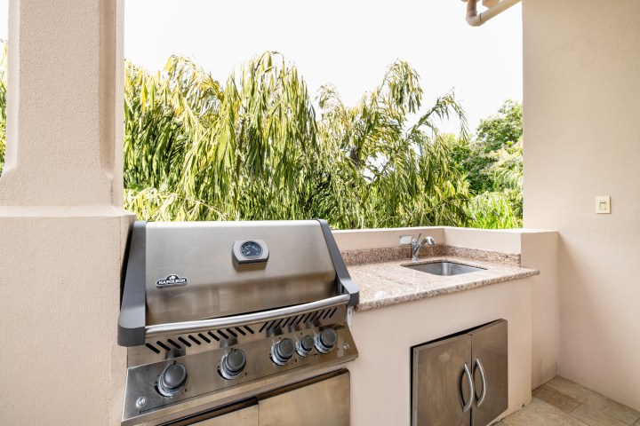 Outdoor kitchen with grill and sink on a balcony overlooking lush greenery.