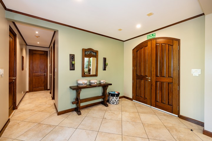 Interior hallway with wooden doors, mirror on wall, and small table with baskets.