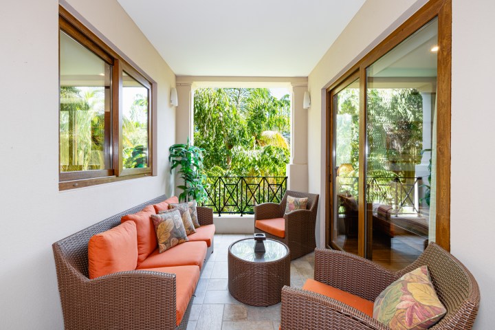 Outdoor patio with orange cushions, wicker furniture, glass table, and green plants.