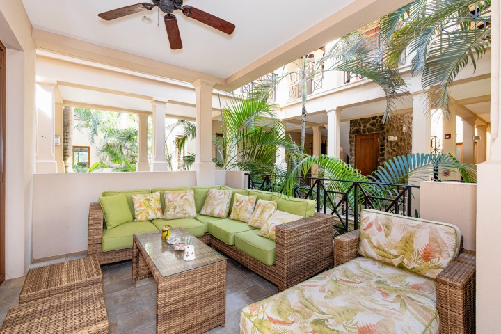Outdoor patio with wicker furniture, green cushions, and tropical plants.