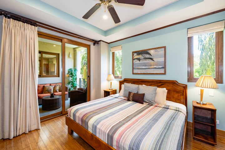Bedroom with striped bedding, wooden furniture, lamps, and sliding doors to a patio with seating.