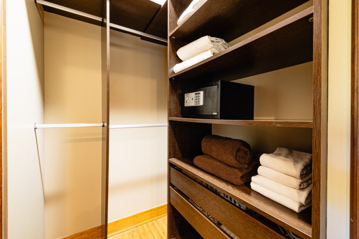 Walk-in closet with shelves holding towels and a safe, and empty hanging rods.
