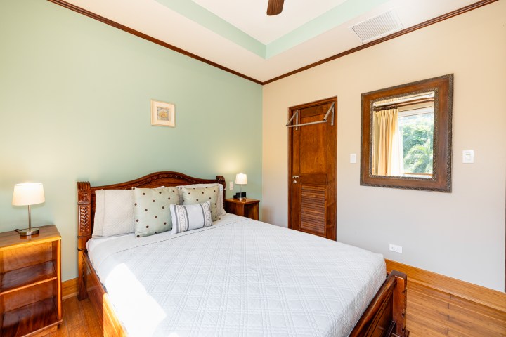 Bedroom with a wooden bed, green accent wall, and a mirror above a wooden door.