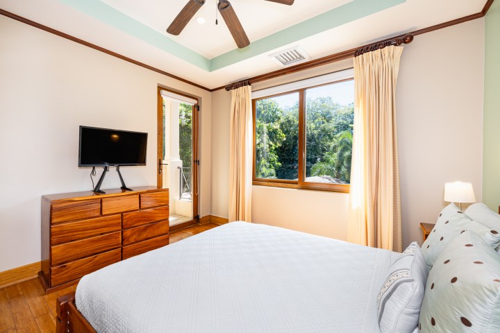 Bedroom with a bed, TV, dresser, window, balcony door, and ceiling fan.