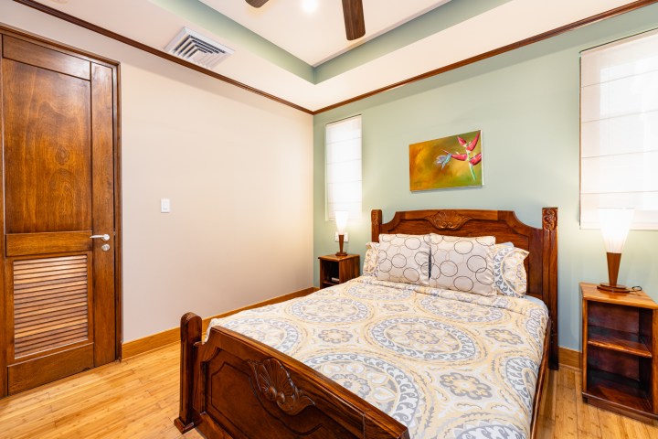 Bedroom with wooden bed, patterned bedding, artwork, and two lamps on nightstands.