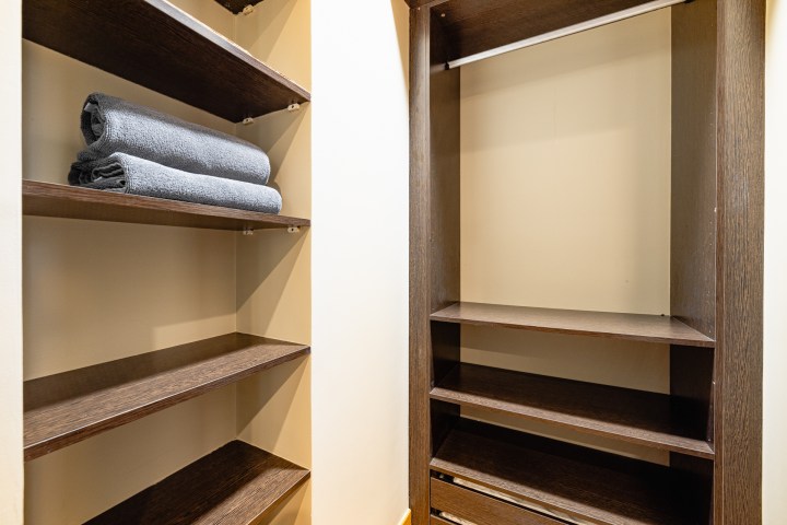 Empty closet with dark wooden shelves and two folded gray towels on a shelf.