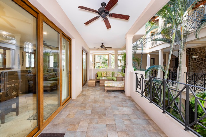 Covered patio with seating area, ceiling fans, and tropical plants in a courtyard setting.