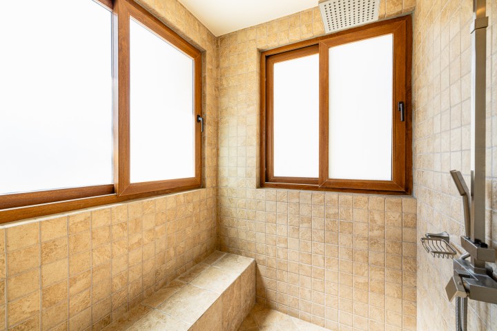 Tiled shower with two frosted windows, bench, and ceiling showerhead.