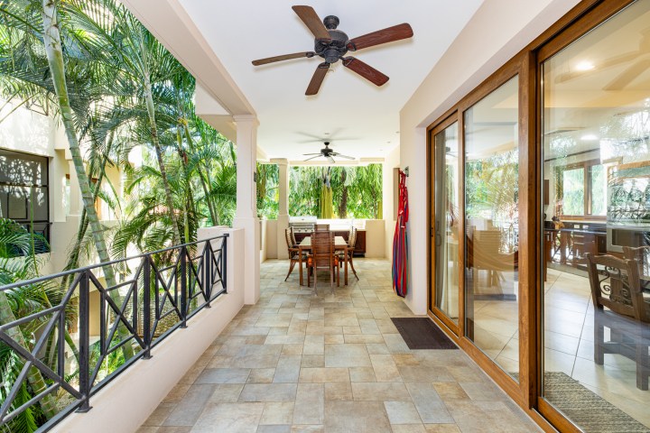 Covered outdoor patio with chairs and tables, surrounded by palm trees, and ceiling fans above.