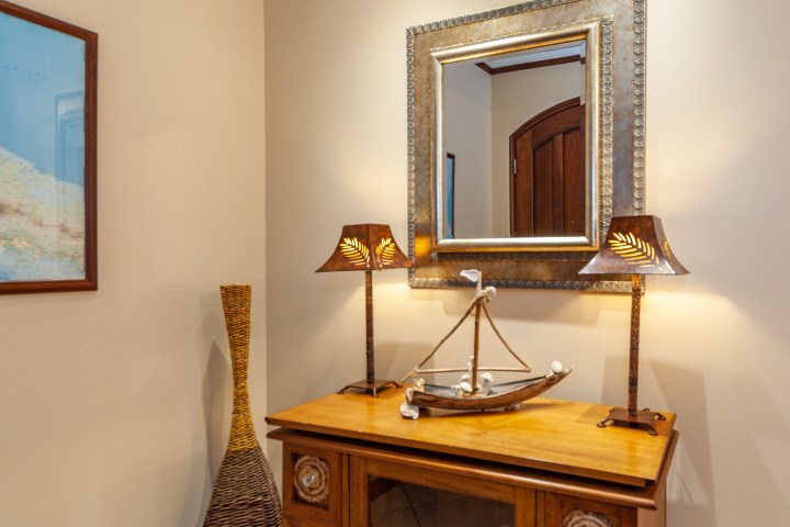 Room corner with a mirror, nautical decor, two lamps, and a tall vase on a wooden table.