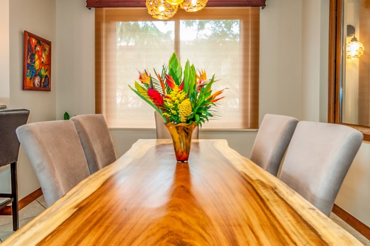 Dining room with a wooden table, vase of tropical flowers, and modern pendant lights.