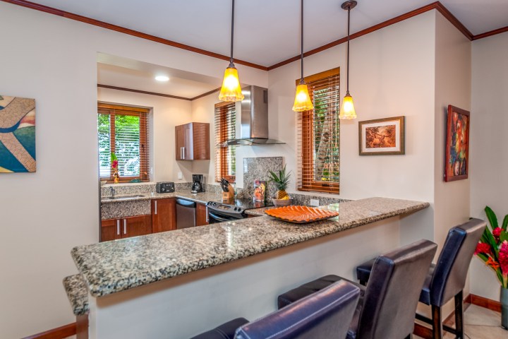 Modern kitchen with granite bar counter, pendant lights, and dark chairs.