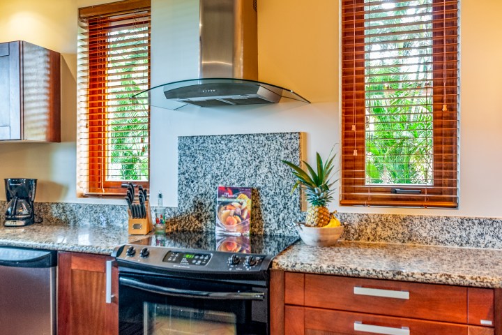 Modern kitchen with granite countertops, fruit bowl, stove, and windows with wooden blinds.
