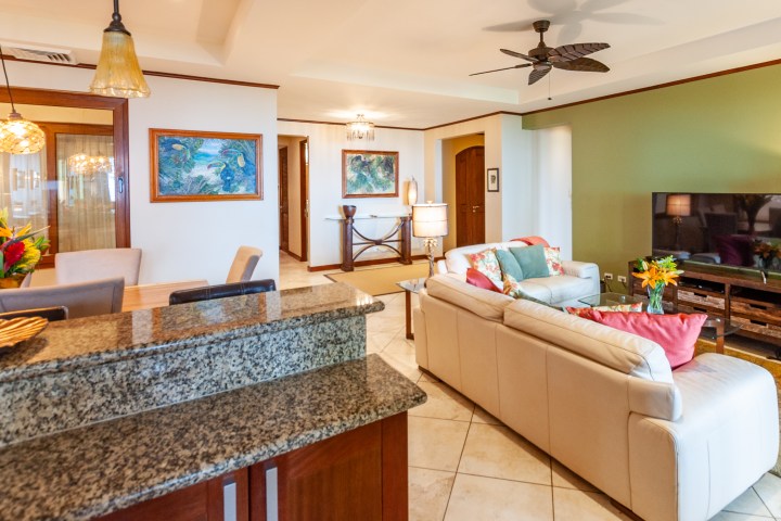 Modern living room with cream sofas, green accent wall, and ceiling fan.