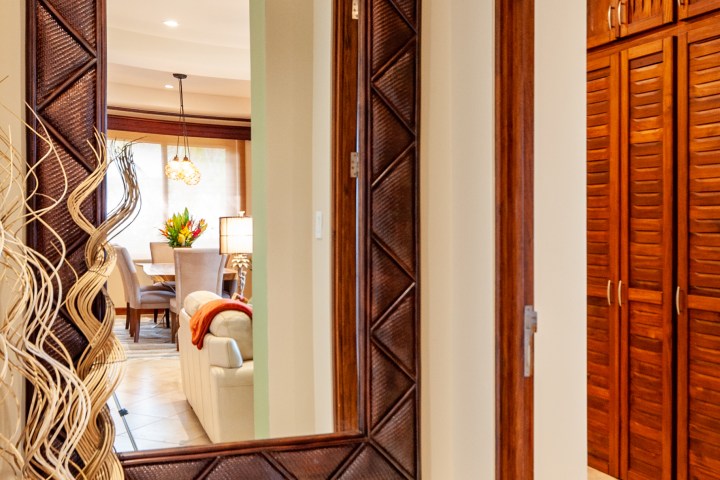 Hallway with decorative mirror, vase, and wooden accents, reflecting a cozy living area with lamps and chairs.