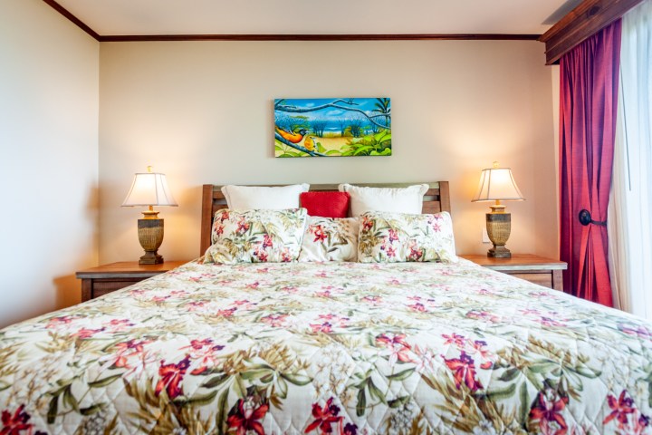 Bedroom with floral bedding, two lamps, and a colorful painting above the bed.