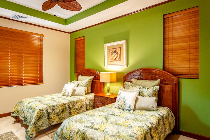 Two twin beds with floral bedding in a room with green walls and wooden blinds.