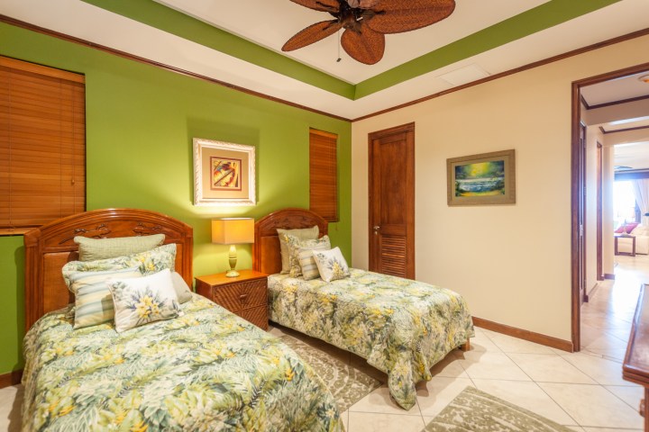 Bedroom with two twin beds, green accent wall, floral bedding, and wooden furniture.