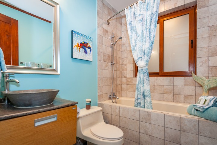 Bathroom with a shower-tub, patterned curtain, sink, and window.