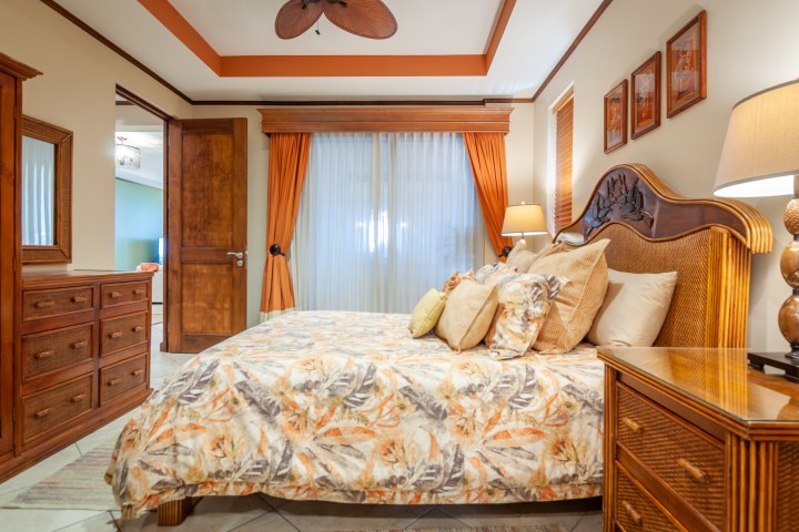 Cozy bedroom with wooden furniture, floral bedding, large window, and decorative ceiling fan.