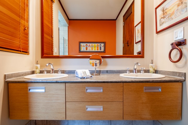 Modern bathroom with dual sinks, large mirror, wood cabinets, and wall art.