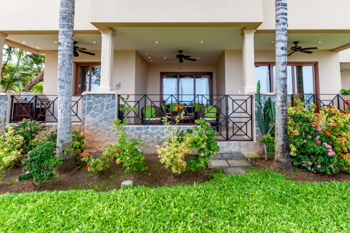 Tropical patio with columns, ceiling fans, and lush garden view.