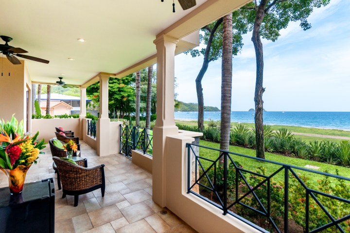 Covered patio with wicker chairs overlooking a beach and ocean view.