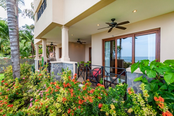 Tropical patio with ceiling fans, sliding glass doors, and vibrant garden, overlooking the ocean.