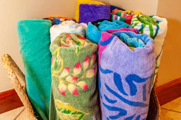 Colorful rolled towels in a woven basket on a tiled floor.