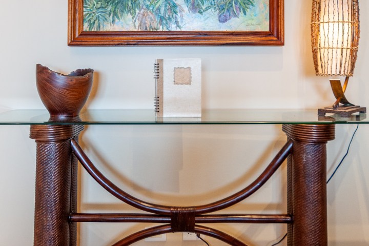 Glass-top table with wooden vase, book, painting, and woven lamp.