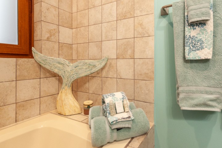 Whale tail sculpture and towels on tub edge in a tiled bathroom corner.