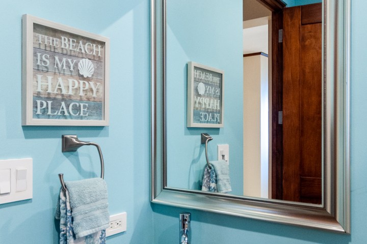 Bathroom with blue walls, a stone sink, silver-framed mirror, and wall art saying 'The beach is my happy place'.