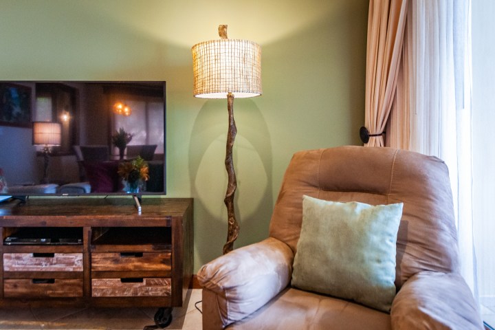 Living room with a TV, wooden cabinet, floor lamp, and beige armchair with a pillow.