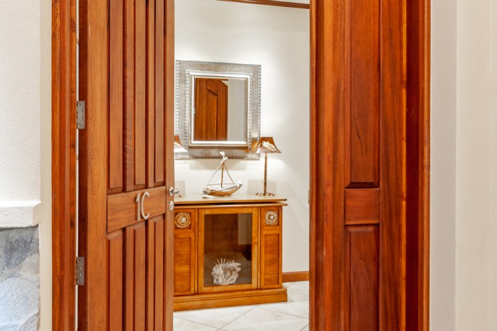 Wooden door opens to hallway with mirror, lamp, and decorative sailboat on cabinet.