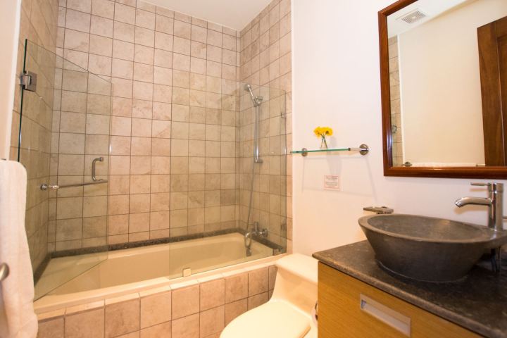 Modern bathroom with tiled shower, glass door, vessel sink, and wooden vanity.