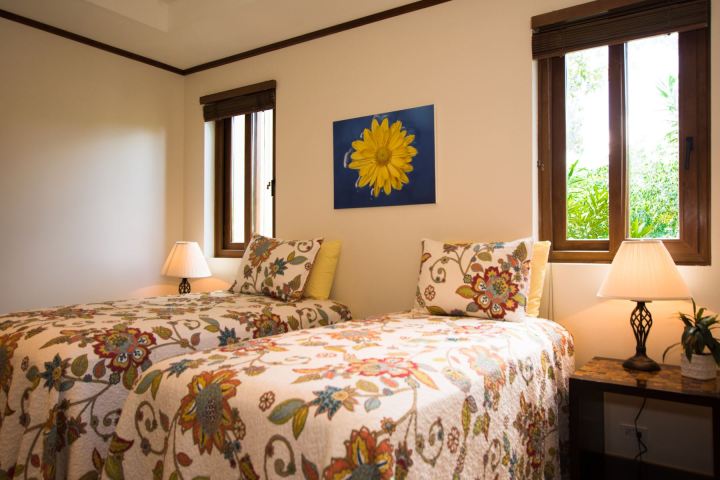 Two twin beds with floral quilts, lamps, and a sunflower painting in a bright room.