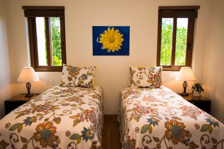 Two beds with floral quilts, lamps on nightstands, windows, and sunflower art on wall.