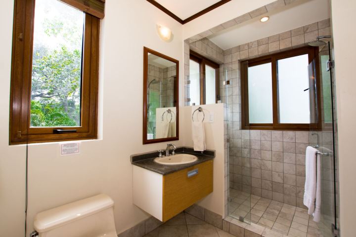 Modern bathroom with tiled shower, wooden windows, and a sink with a mirror.